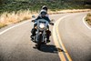 Front angle of a person and passenger riding a motorcycle on a road.