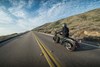 Three-quarter rear angle of a person riding a motorcycle on a road.