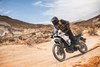 Three-quarter front angle of a person riding a motorcycle on a dirt trail.