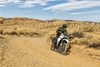 Three-quarter front angle of a person riding a motorcycle on a dirt trail.