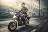 Three-quarter front angle of a person riding a motorcycle on a street.