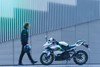 Side angle of a person approaching a parked motorcycle.