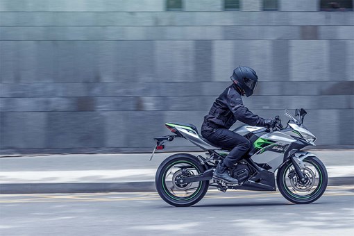 Side angle of a person riding a green motorcycle on a street. opens in a new window