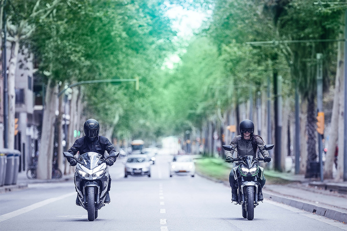 Front angle of two people riding motorcycles on a street.