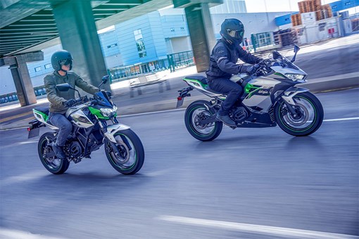 Three-quarter front angle of two people riding motorcycles on a road. opens in a new window