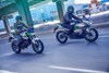 Three-quarter front angle of two people riding motorcycles on a road.