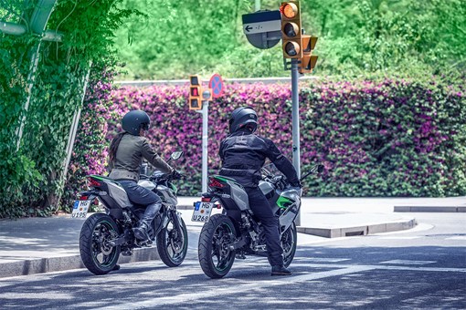 Three-quarter rear angle of two people on motorcycles stopped at a red light. opens in a new window