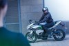 Side angle of a person on a parked motorcycle looking over their shoulder.