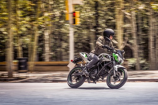 Side angle of a person riding a green motorcycle on a street. opens in a new window