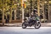 Side angle of a person riding a green motorcycle on a street.