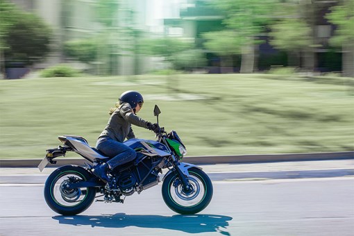 Profile angle of a person riding a green motorcycle on a street. opens in a new window