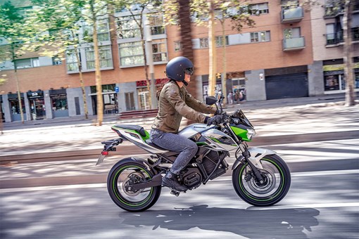 Side angle of a person riding a green electric motorcycle on a street. opens in a new window