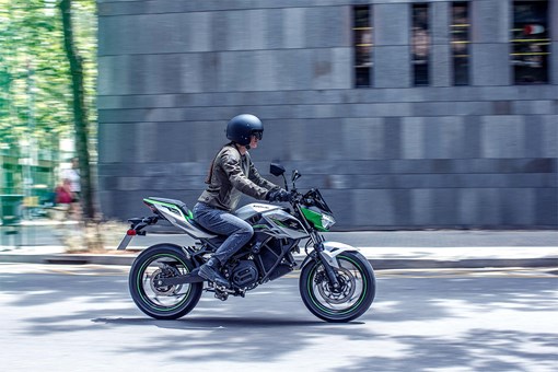 Side angle of a person riding a green electric motorcycle on a road. opens in a new window