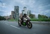 Three-quarter front angle of a person riding a motorcycle on a city street.