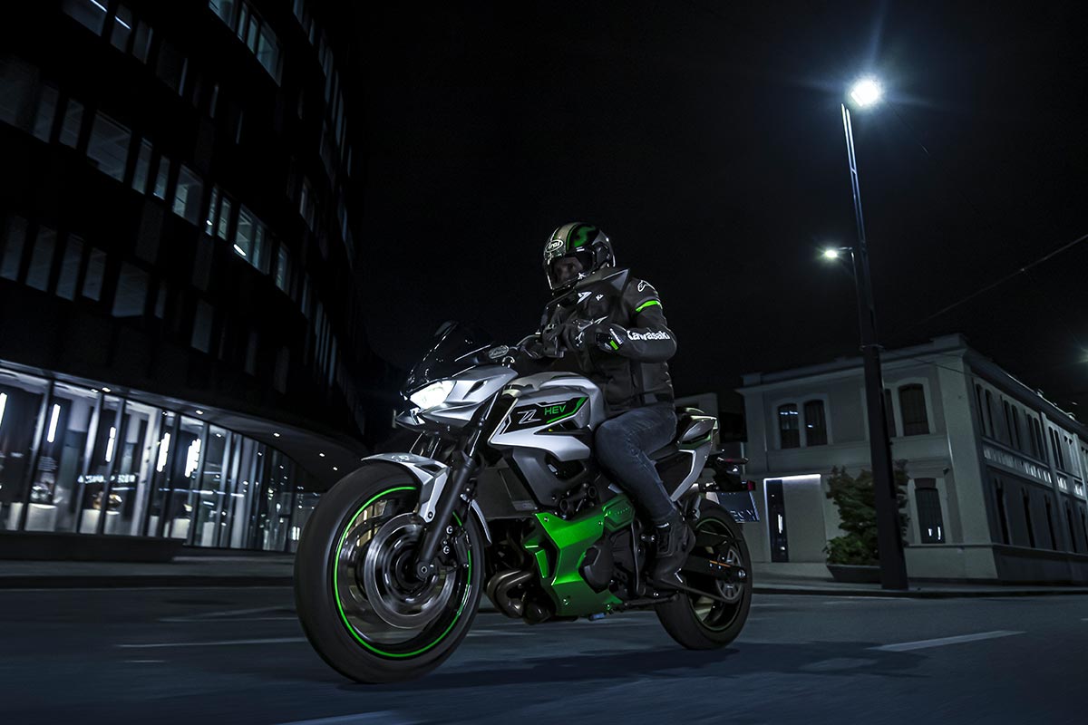 Three-quarter front angle of a person riding a motorcycle on a city street at night.