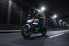 Three-quarter front angle of a person riding a green motorcycle on a city street.