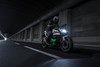 Three-quarter front angle of a person riding a motorcycle in a city at night.