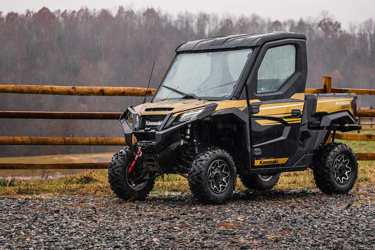 Three-quarter front angle of a side x side parked next to a fence.