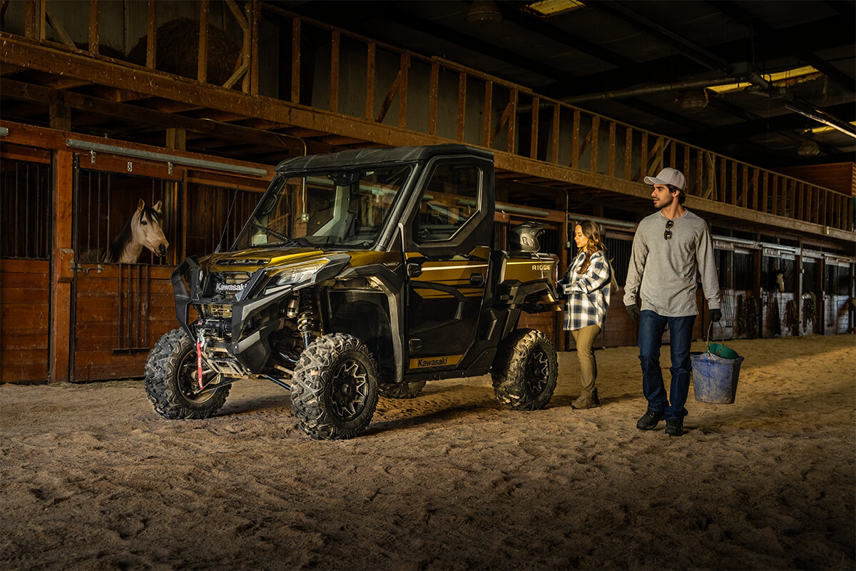 Three-quarter front angle of a side x side parked in a barn near horses.