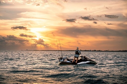 Side angle of a person standing on a personal watercraft at sunset. opens in a new window
