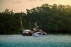 Side angle of a person fishing on a personal watercraft in the water.
