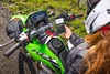 Three-quarter rear angle of a person sitting on a parked motorcycle looking at their phone.