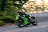 Side angle of a person riding a green motorcycle on a road.