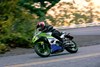 Three-quarter front angle of a person riding a motorcycle on a road.