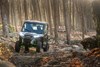 Front angle of two people riding a side x side through woods.