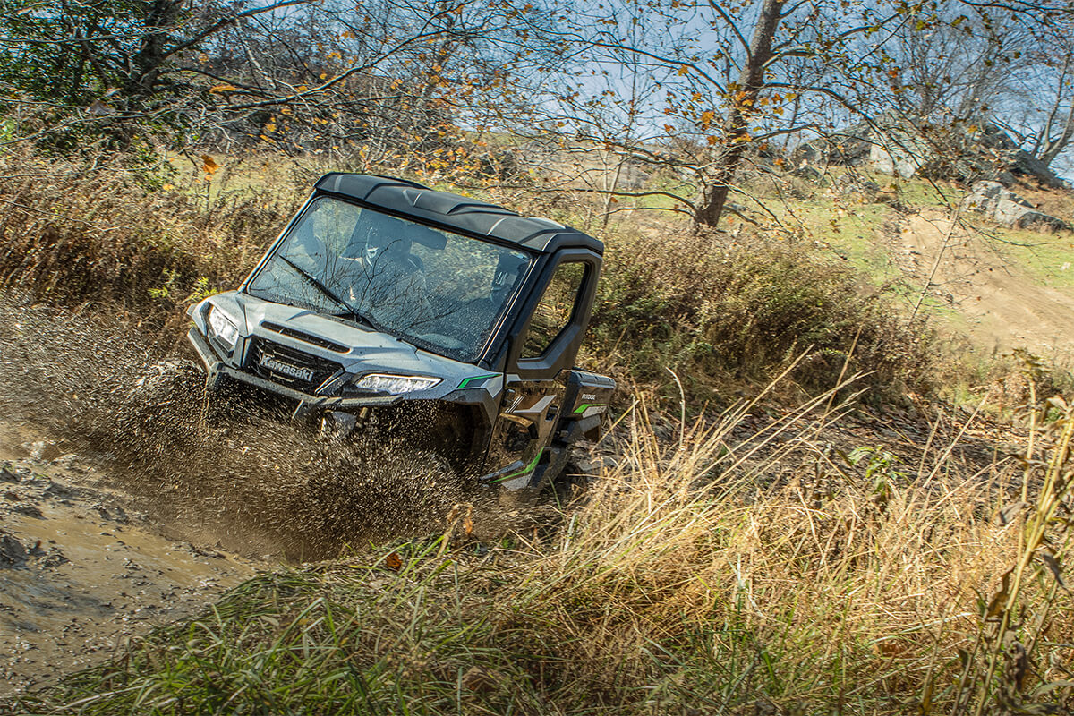 Front angle of two people riding a side x side through muddy water.