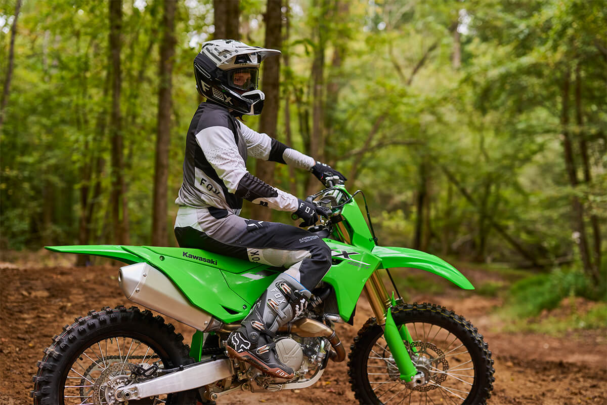 Side angle of a person standing next to a parked motorcycle off-road.