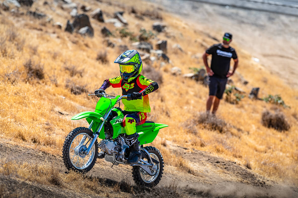Three-quarter front angle of a person riding a motorcycle up an off-road hill.