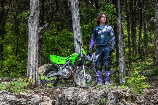 Front angle of a person standing next to a motorcycle with trees in the background. opens in a new window