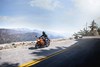 Three-quarter front angle of a person riding a motorcycle on a mountain highway.
