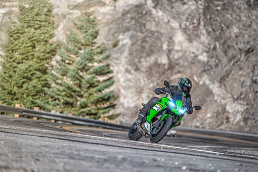 Three-quarter front angle of a person riding a green motorcycle on a highway. opens in a new window