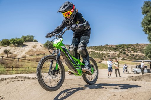 Three-quarter front angle of a young adult riding an electric balance bike on dirt. opens in a new window