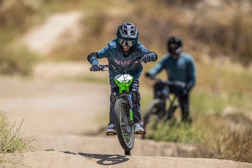 Front angle of a young adult riding an electric balance bike over small dirt bumps. opens in a new window