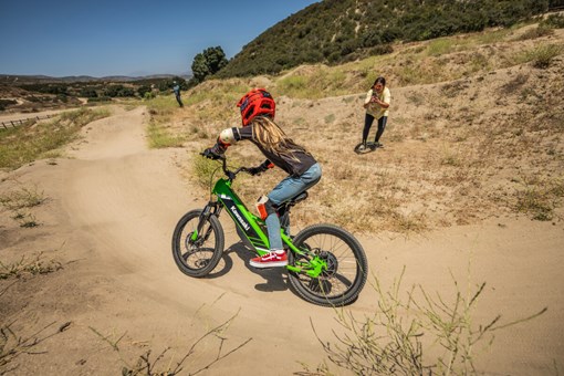 Three-quarter rear angle of a young adult riding an electric balance bike around a corner.  opens in a new window