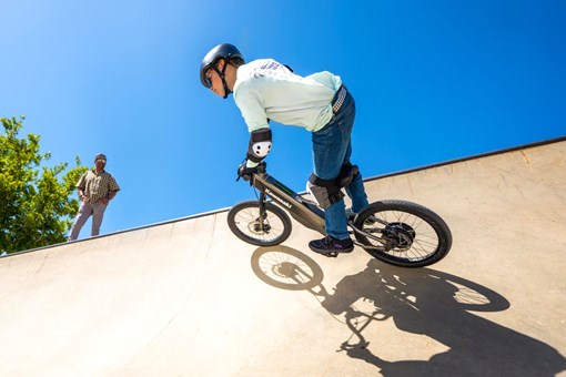 Three-quarter rear angle of a young adult riding an electric balance bike up the outer edge of the skate park. opens in a new window