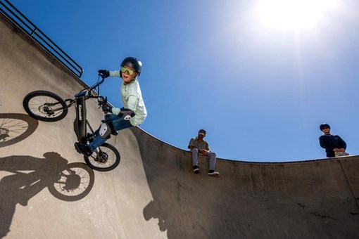 Upward side angle of a young adult riding an electric balance bike around a large turn. opens in a new window