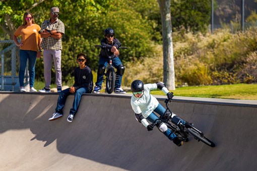 Front angle of a young adult riding an electric balance bike with friends in the background. opens in a new window