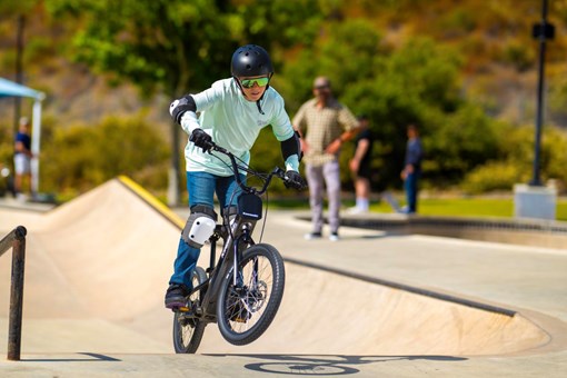 Three-quarter front angle of a young adult riding an electric balance bike in a skate park. opens in a new window