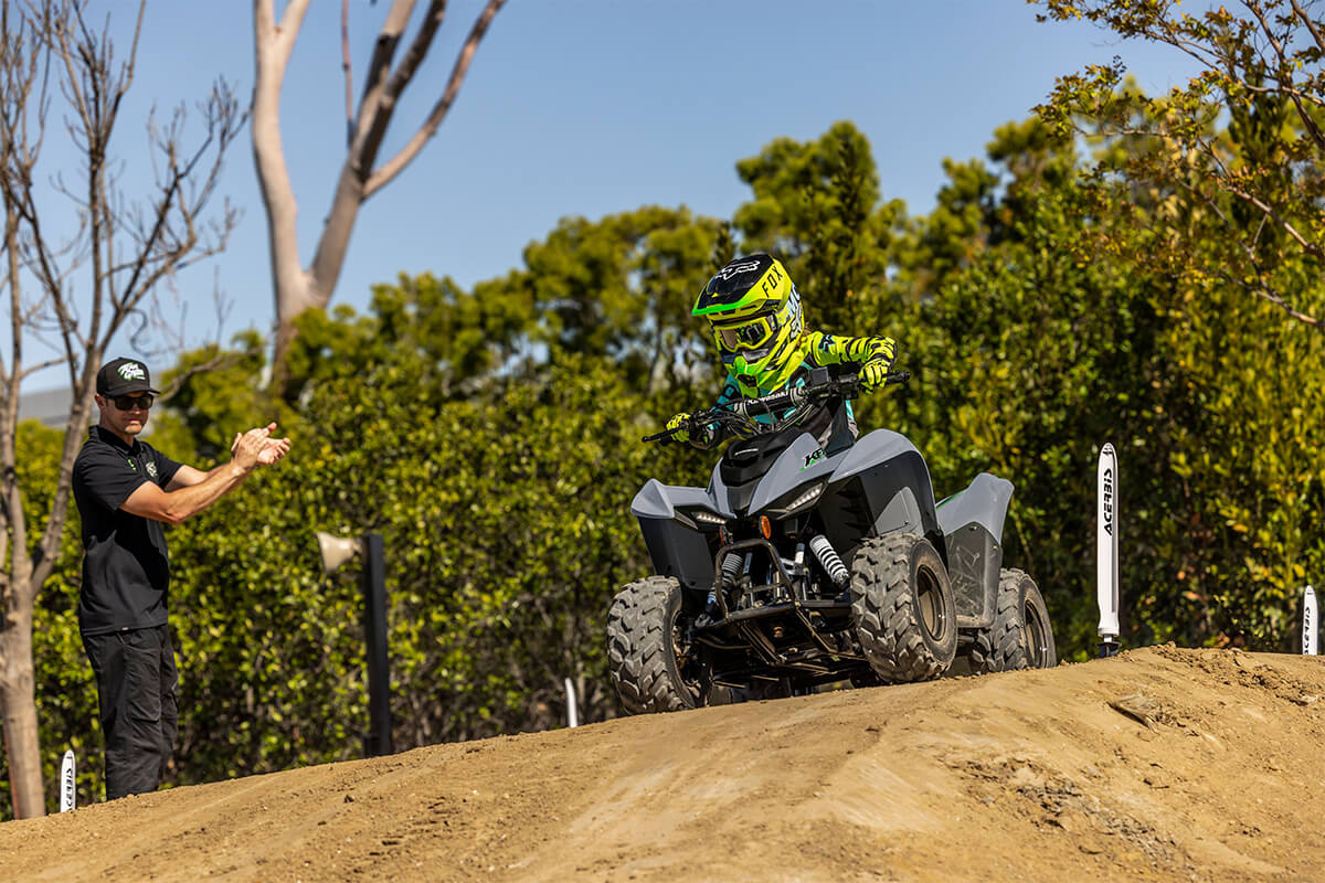Three-quarter front angle of a person riding a gray ATV off-road.