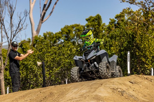 Three-quarter front angle of a person riding a gray ATV off-road. opens in a new window