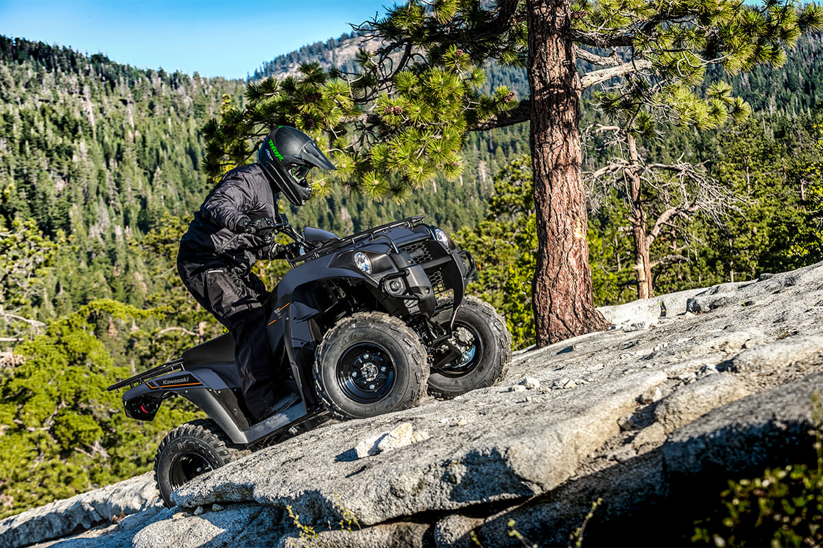 Three-quarter front angle of a person riding an ATV up a rocky mountain.