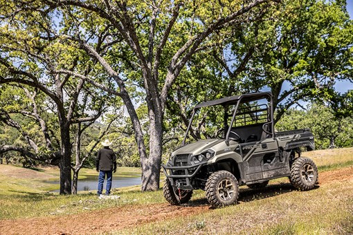 Three-quarter front angle of a person standing next to a parked side x side off-road. opens in a new window