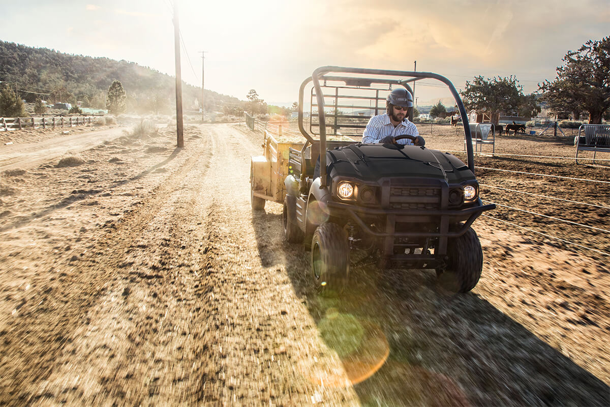 Three-quarter front angle of a person driving a side x side on a dirt road.