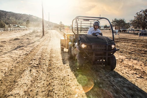 Three-quarter front angle of a person driving a side x side on a dirt road. opens in a new window