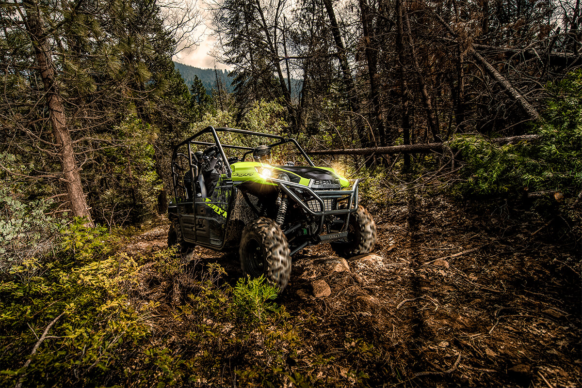 Three-quarter front angle of a person driving a side x side through the woods.