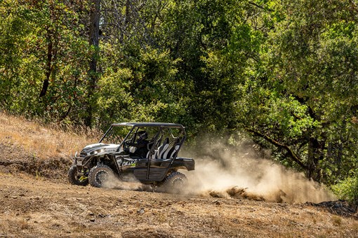 Three-quarter front angle of a person driving a side x side on a dirt trail. opens in a new window